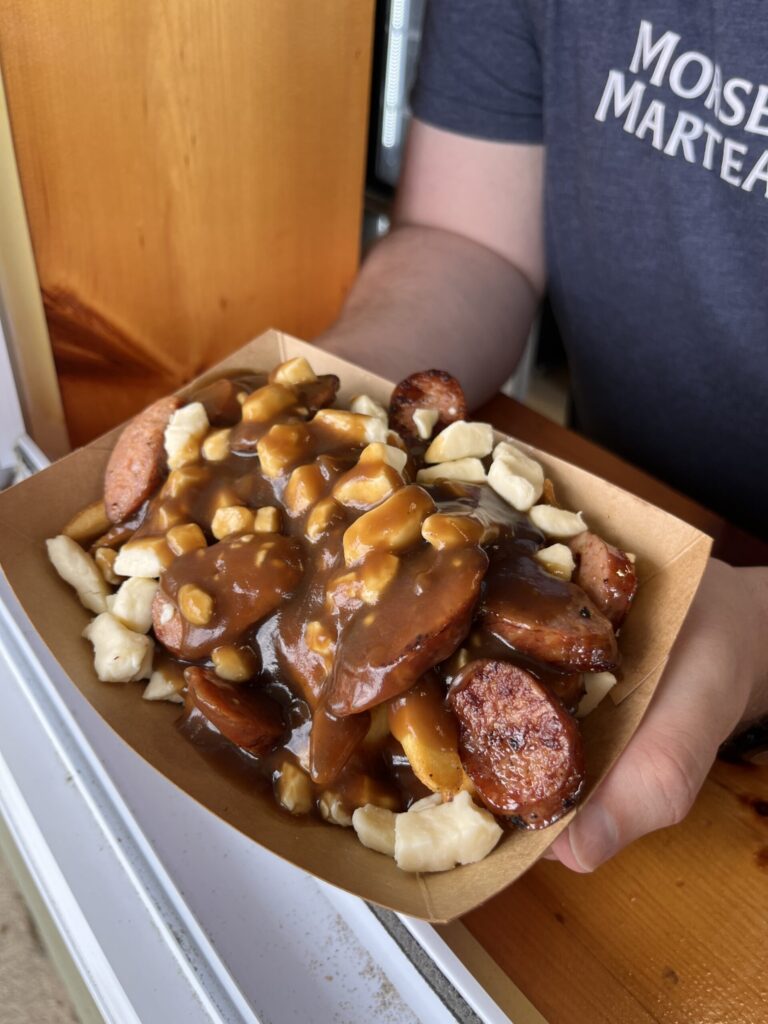 A canteen worker holding a smoked sausage poutine at the window at the Parlee Beach East Canteen